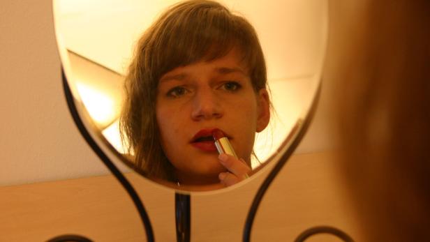 Eine Frau trägt vor einem Spiegel roten Lippenstift auf.