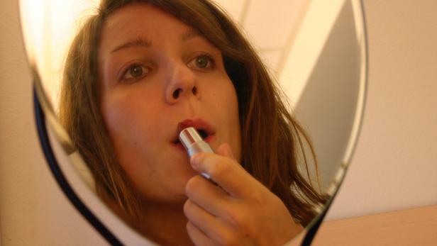 Eine junge Frau trägt Lippenstift vor einem Spiegel auf.