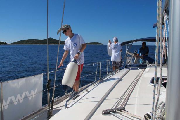 Zwei Jugendliche hantieren mit Fendern auf einem Segelboot auf dem Meer.