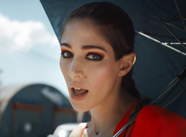 Eine Frau mit auffälligem orangefarbenem Make-up steht unter einem Regenschirm.