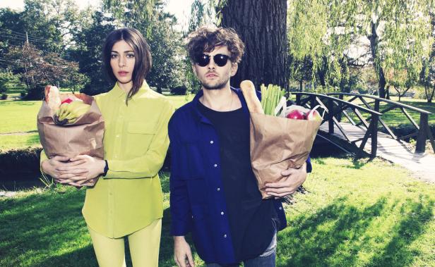 Ein Mann mit Sonnenbrille und eine Frau halten Einkaufstüten in einem Park.