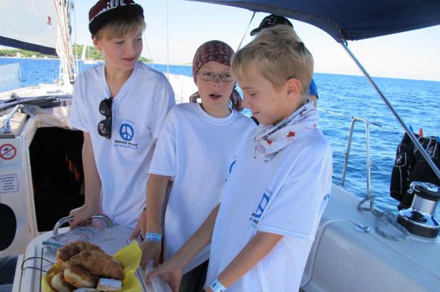 Drei Jugendliche auf einem Segelboot betrachten Gebäck.