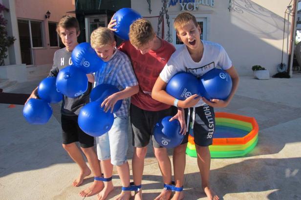 Vier Jungen balancieren blaue Bälle mit Händen und Füßen vor einem Gebäude.