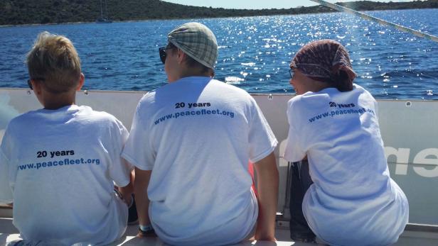 Drei Kinder sitzen auf einem Boot und blicken auf das Meer.