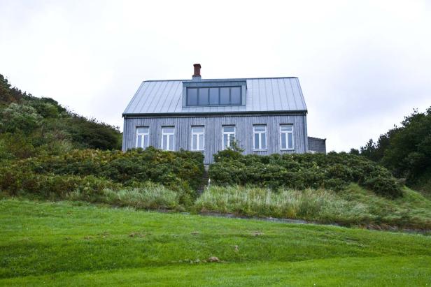 Ein graues Holzhaus mit Metalldach steht auf einem grünen Hügel.
