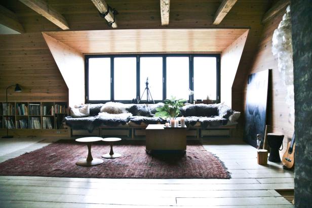 Ein Wohnzimmer mit Holzbalkendecke, großem Fenster und einem Sofa mit Fellbezug.