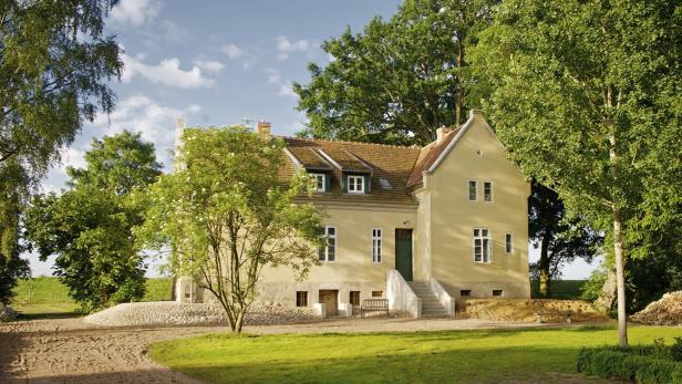 Ein gelbes Landhaus mit einem grünen Garten und Bäumen im Sommer.