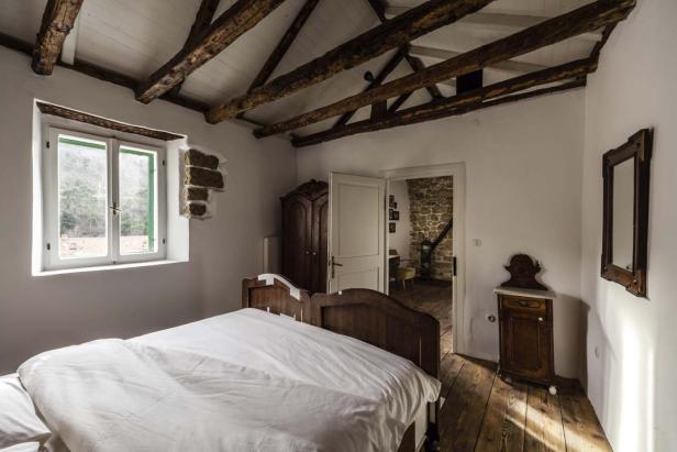 Ein Schlafzimmer mit Holzbalkendecke, Holzboden und einem Bett mit weißer Bettwäsche.