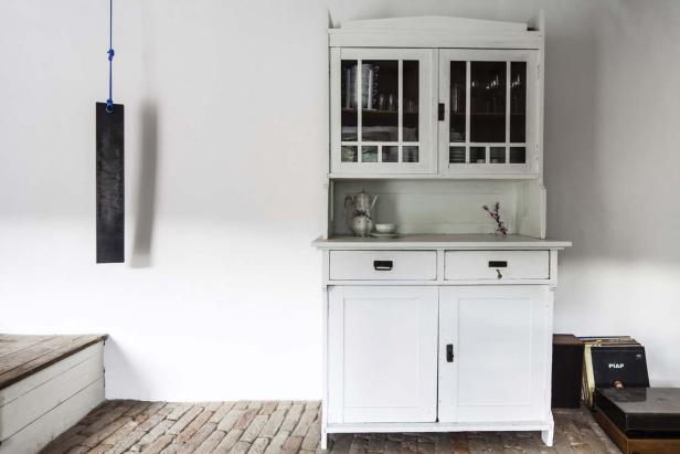 Ein weißer Schrank steht in einem Zimmer mit Ziegelboden.