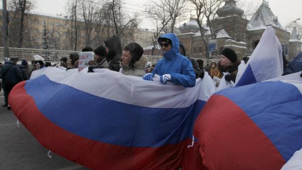 Menschen tragen eine große russische Flagge bei einer Demonstration.
