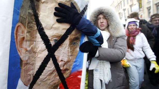 Eine Frau hält ein Plakat mit einem durchgestrichenen Porträt von Wladimir Putin bei einer Demonstration.