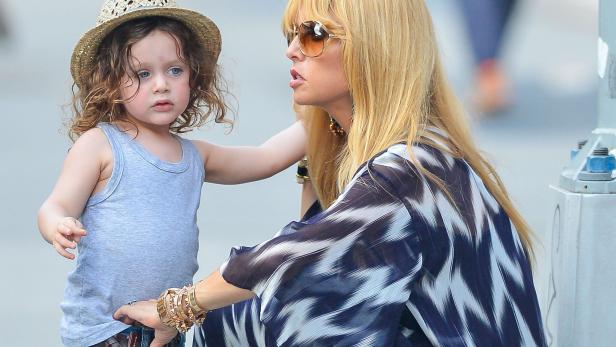 Eine Frau mit blonden Haaren und Sonnenbrille steht neben einem kleinen Jungen mit Hut.