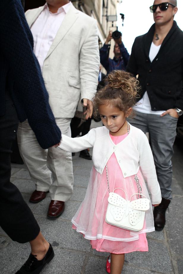 Ein kleines Mädchen in einem rosa Kleid und mit einer Schmetterlingstasche geht an der Hand eines Erwachsenen.