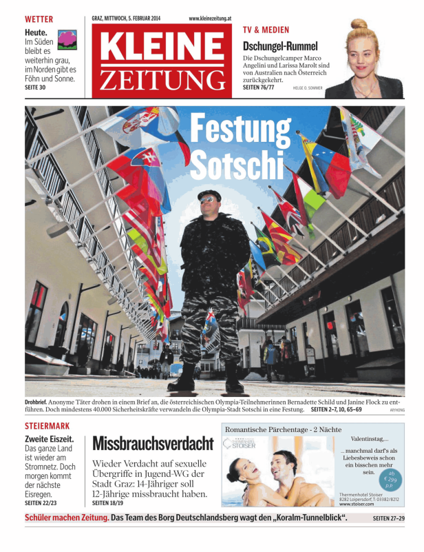 Ein Mann steht vor einer Reihe von Flaggen mit dem Schriftzug „Festung Sotschi“.