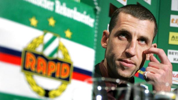 Ein Mann steht vor einem Banner des Fußballvereins Rapid Wien.