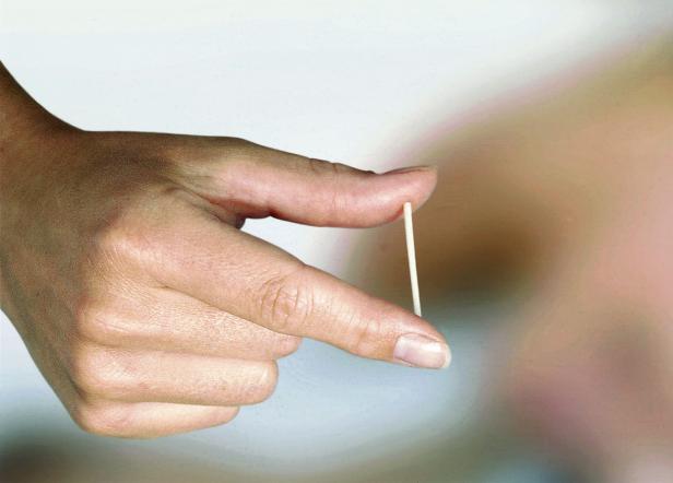Eine Hand hält einen dünnen, weißen Gegenstand zwischen Daumen und Zeigefinger.