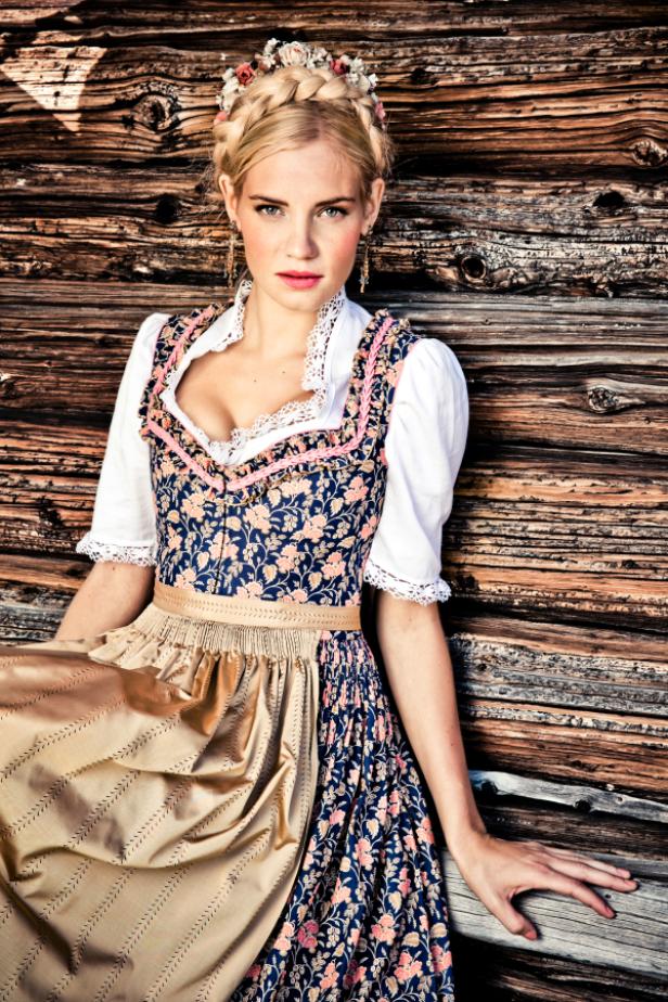 Eine Frau im Dirndl posiert vor einer Holzwand.