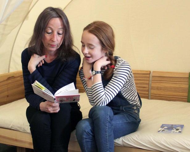 Eine Frau liest einem Mädchen auf einem Bett ein Buch vor.