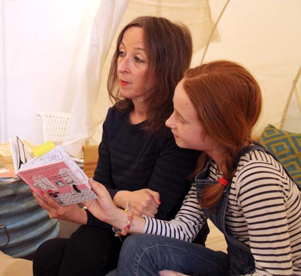 Eine Frau und ein Mädchen sitzen zusammen und betrachten ein aufgeschlagenes Buch mit Illustrationen.