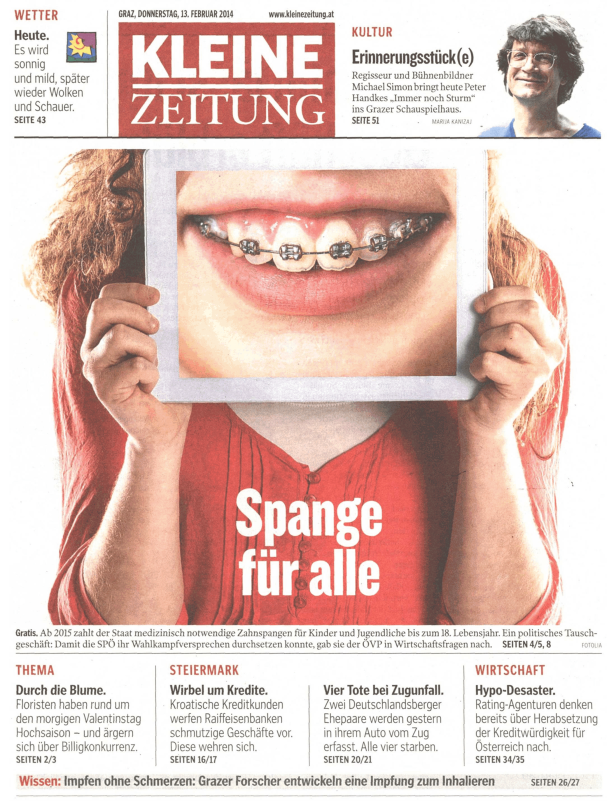 Eine Person hält ein Bild von einem Mund mit Zahnspange hoch. Auf dem roten T-Shirt steht „Spange für alle“.