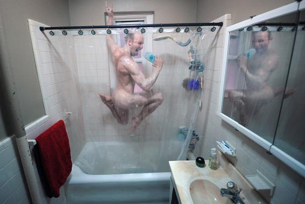 Ein Mann springt nackt unter der Dusche und singt in eine Shampooflasche.