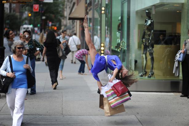 Eine Frau macht einen Handstand mit Einkaufstüten auf einem Bürgersteig.