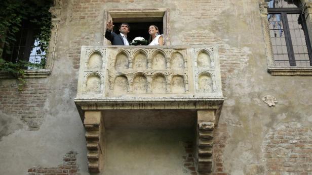 Ein frisch vermähltes Paar winkt von einem steinernen Balkon.