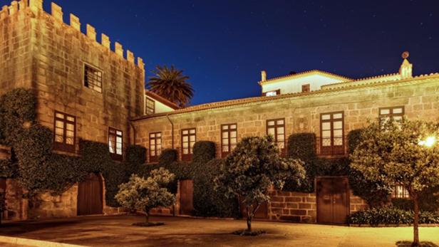 Ein beleuchtetes Steingebäude mit Efeu und Bäumen unter einem Nachthimmel.