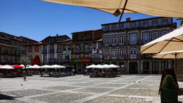 Ein belebter Platz in Guimarães, Portugal, mit Restaurants und historischen Gebäuden.