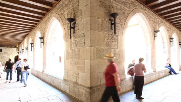 Menschen gehen durch einen hellen Gang mit Steinbögen und Wandleuchten.