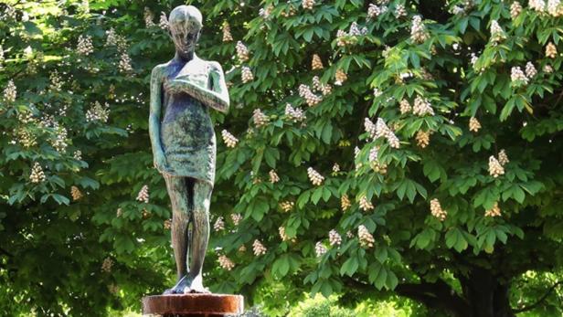 Eine Bronzestatue einer jungen Frau vor einem blühenden Baum.