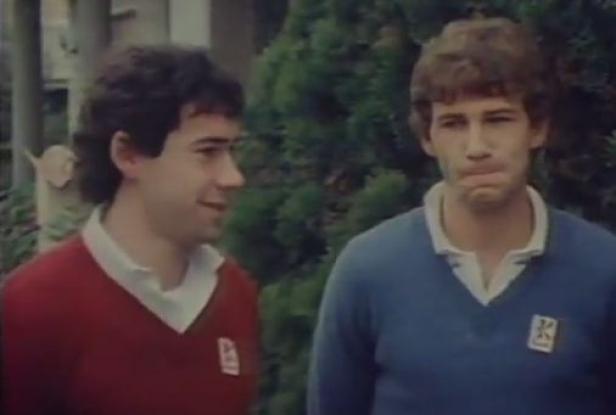 Zwei junge Männer stehen nebeneinander und tragen Pullover mit einem Logo.