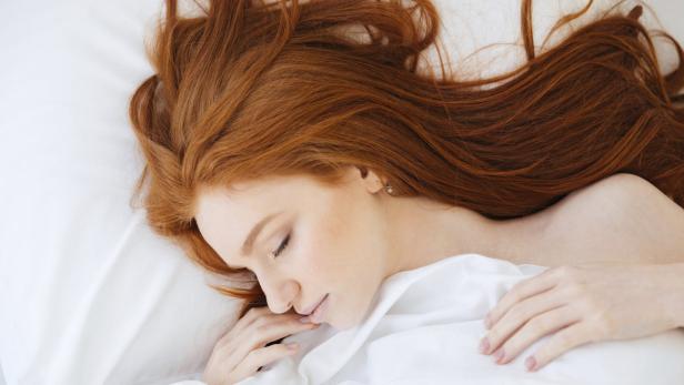 Eine rothaarige Frau schläft in einem weißen Bett.