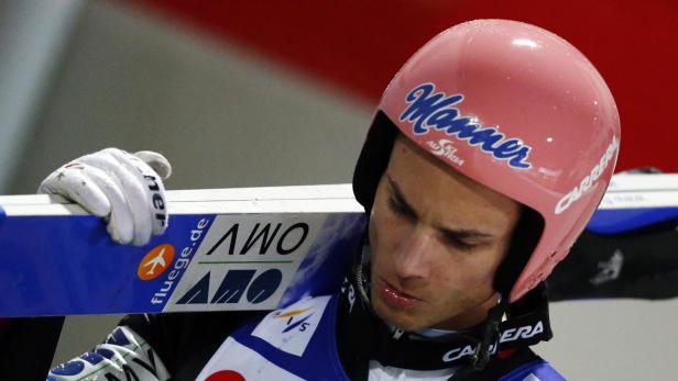 Ein Skispringer mit Helm und Skiern auf der Schulter.