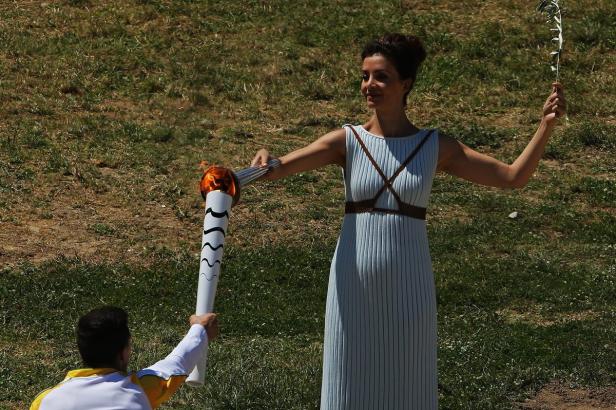 Eine Frau im Kleid nimmt die olympische Fackel entgegen.