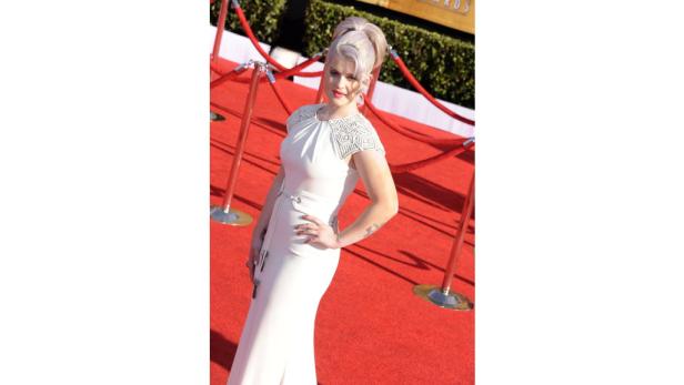 Kelly Osbourne posiert auf dem roten Teppich in einem weißen Kleid.