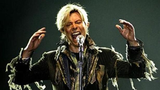 David Bowie singt mit erhobenen Händen in ein Mikrofon.