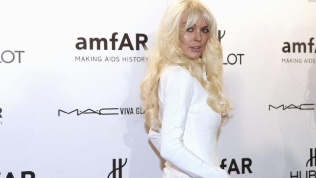Lindsay Lohan posiert vor einer Wand mit Logos von amfAR und MAC.