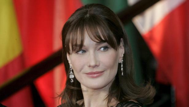 Ein Porträt von Carla Bruni mit Ohrringen vor einem Hintergrund aus Flaggen.