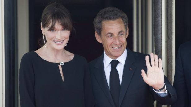 Carla Bruni-Sarkozy und Nicolas Sarkozy lächeln in die Kamera und winken.