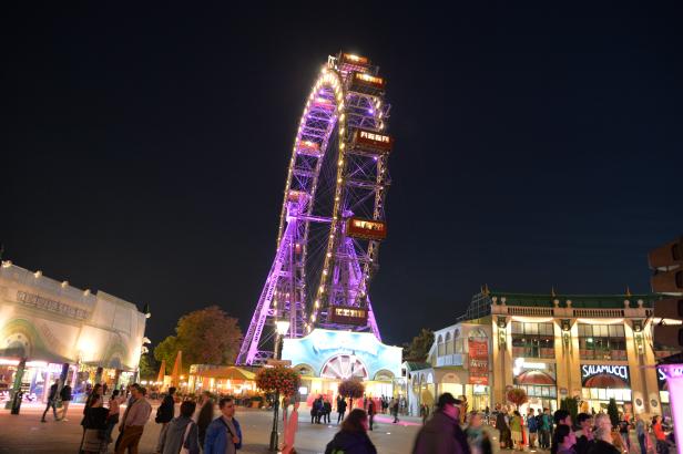 Das Wiener Riesenrad ist nachts hell erleuchtet und von Menschen umgeben.
