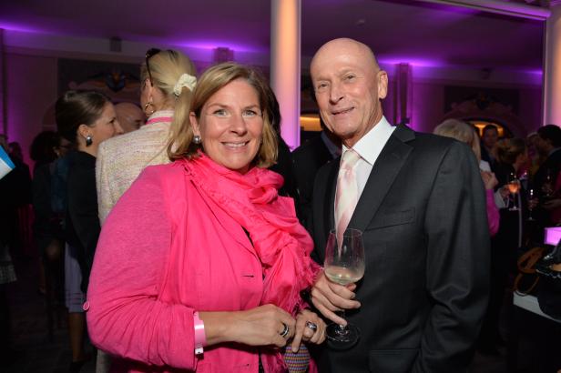 Eine Frau in Pink und ein Mann im Anzug posieren mit einem Weinglas.