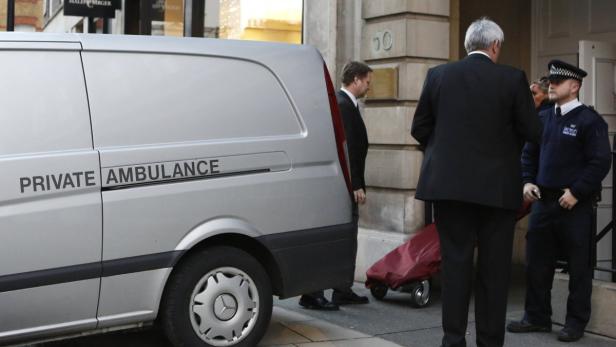 Ein Krankenwagen steht vor einem Gebäude, bewacht von einem Polizisten.