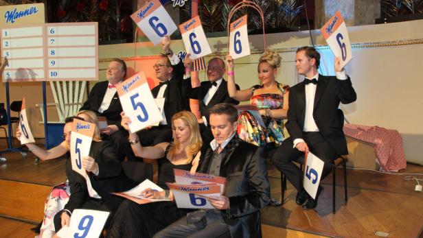 Eine Gruppe von Juroren bewertet eine Darbietung und hält Wertungstafeln mit den Zahlen 5, 6 und 9 hoch.