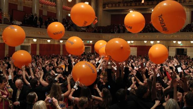 Eine Menschenmenge in einem Ballsaal mit orangen „Aperol“-Luftballons.