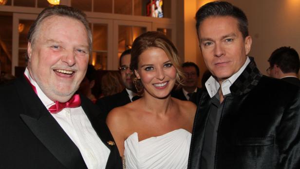 Drei Personen posieren für ein Foto, darunter eine Frau in einem weißen Kleid.