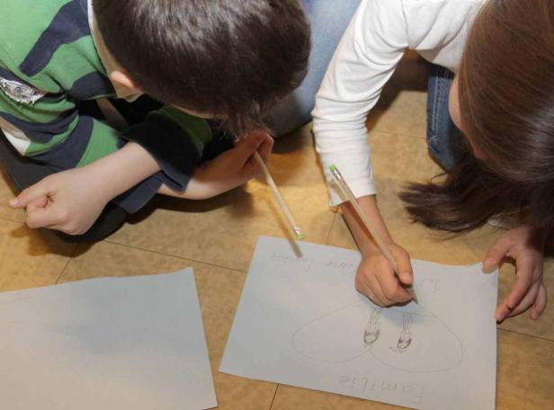 Zwei Kinder zeichnen gemeinsam ein Bild mit der Aufschrift „Familie“.