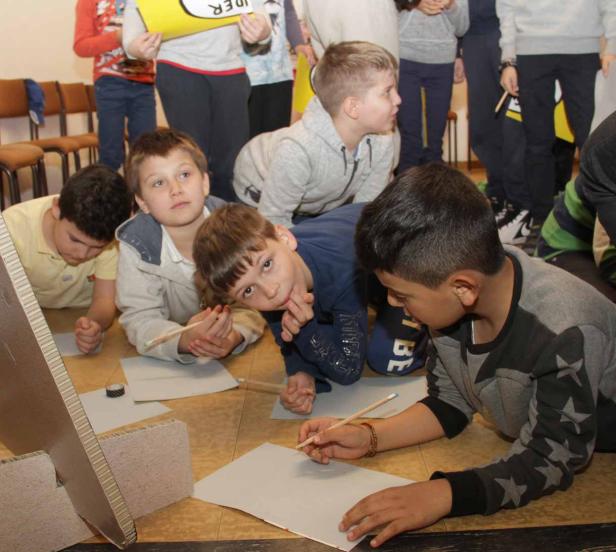 Eine Gruppe von Jungen liegt auf dem Boden und zeichnet auf Papier.