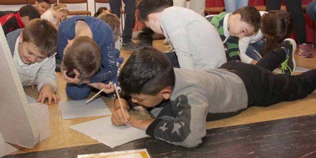 Mehrere Kinder liegen auf dem Boden und zeichnen auf Papier.