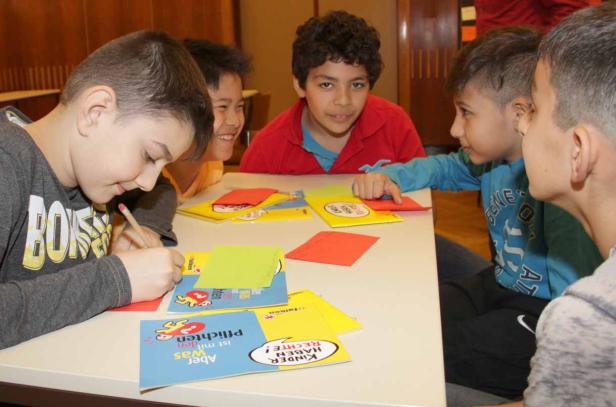 Eine Gruppe von Kindern sitzt an einem Tisch und arbeitet an bunten Heften.